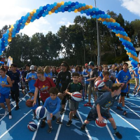 A group of children bouncing balls on a track with a balloon banner arch in the background
