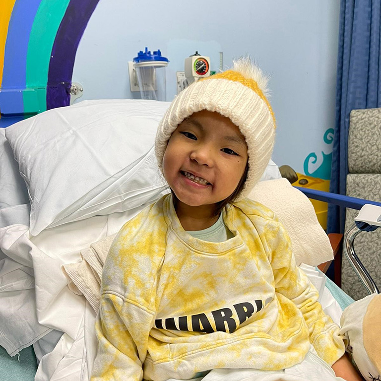 a girl in a stocking cap smiling in a hospital bed