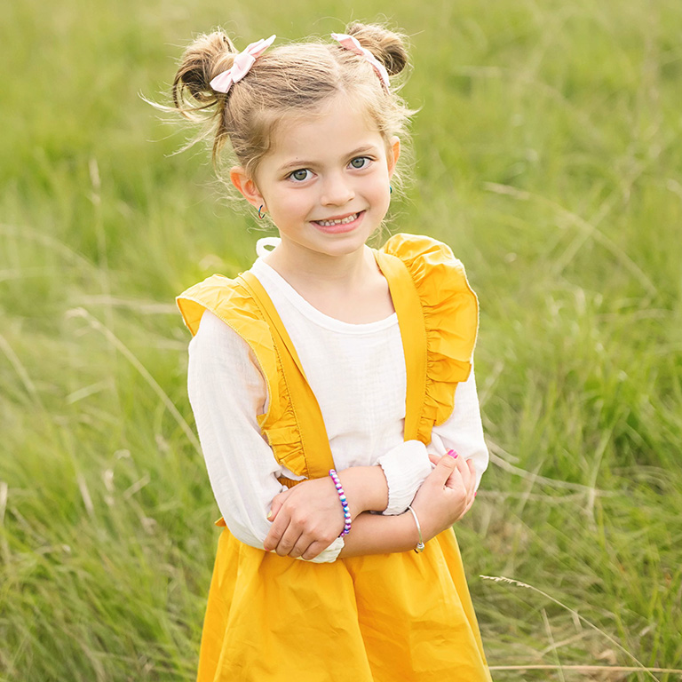 A girl in a yellow dress standing in green field.