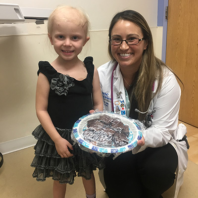 A doctor kneeling next to her young patient holding a tray of baked goods.