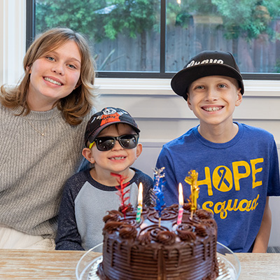 An adult and 2 children smiling with a birthday cake in front of them.