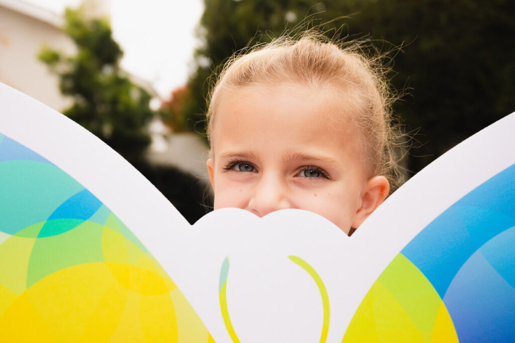 A child peaking out behind a Pediatric Cancer Research Sign.