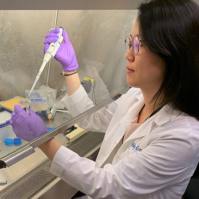 Dr Chen in a labcoat and gloves working in her lab.