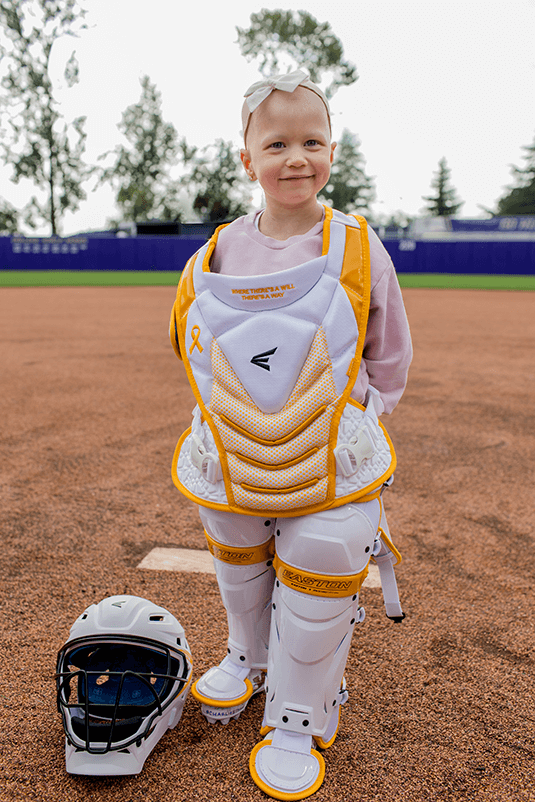 A young girl wearing Jen Shro's Lacrosse Catching gear with a Pediatric Cancer Research Foundation Theme