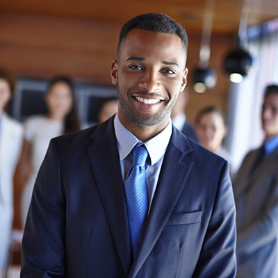 A man wearing a suit with work colleagues in the background.