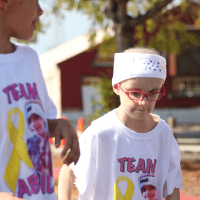 A young child with cancer walking with her friends. They are all wearing matching Team Abigail tshirts.